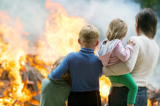 a mother and her three children holding on to each other as a fire burns a building before them