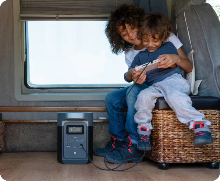 two children sitting on a storage container sharing a gaming device connected to an EcoFlow off grid power station